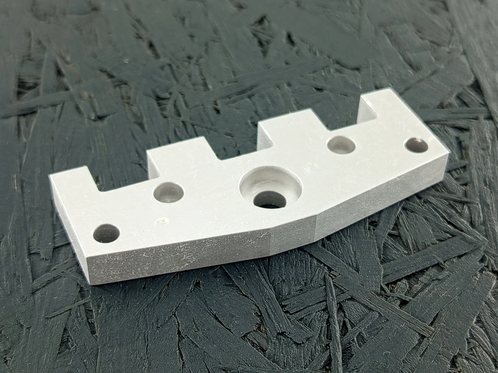 Nahaufnahme eines silbernen, CNC-gefrästen Flansches aus Aluminium 5083 mit Senkung, Bohrungen und komplexer Kontur auf dunklem Hintergrund.