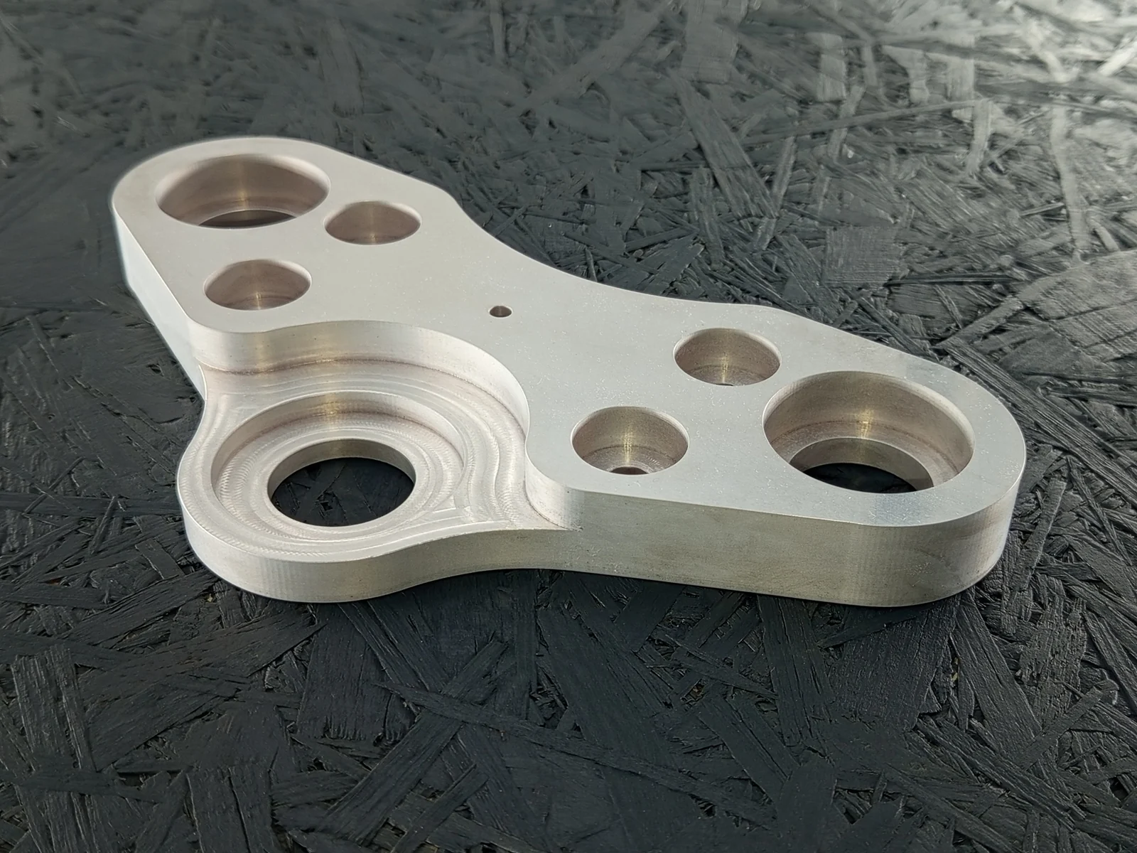CNC-gefräster Halter aus Alu 7075, 20mm dick, mit Taschen und Bohrungen auf dunklem Hintergrund.