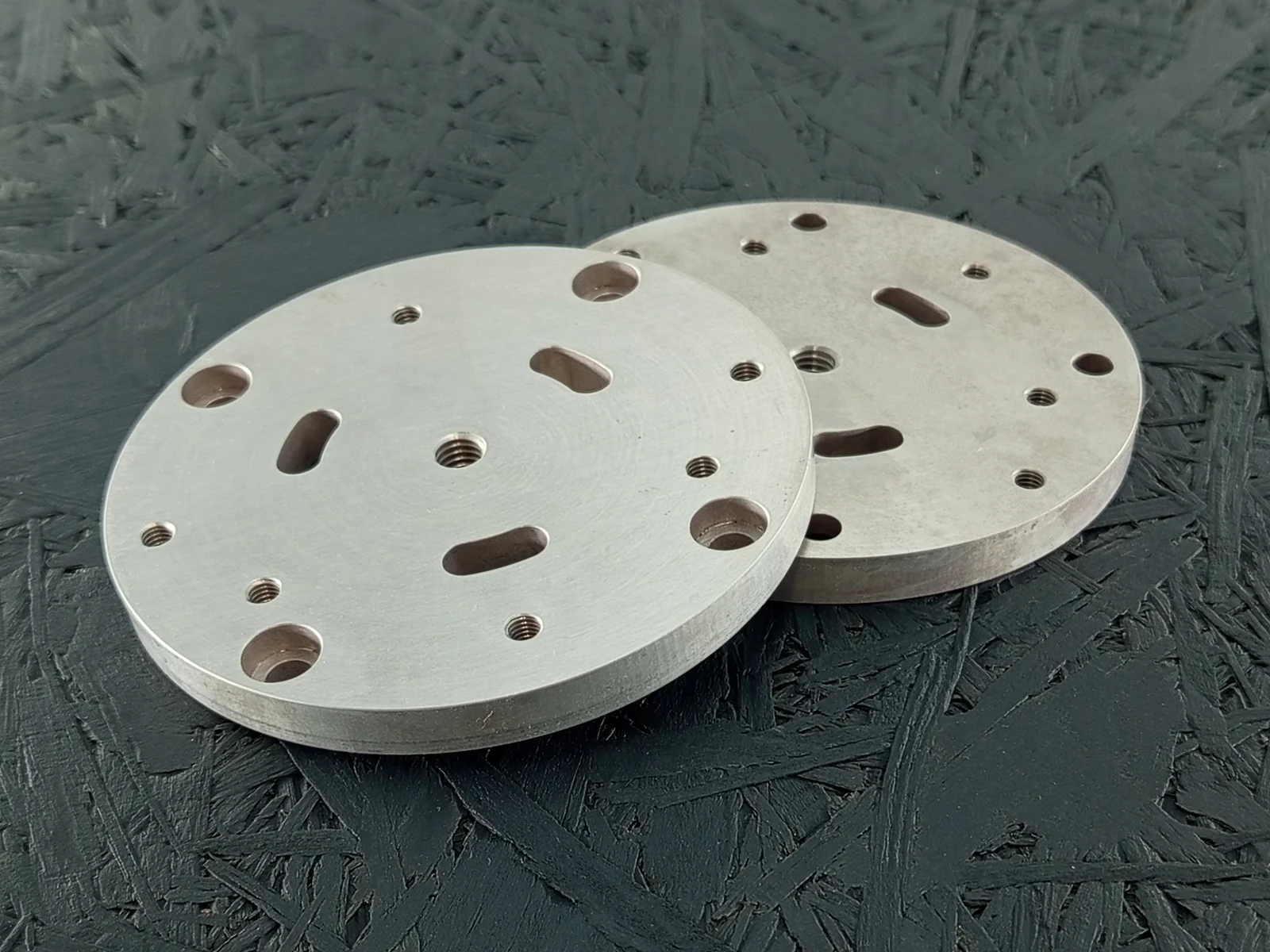Zwei CNC-gefräste runde Montageplatten aus Alu 7075, 8mm dick, mit Gewinden, Senkungen, Bohrungen und Langlöchern auf dunklem Hintergrund.