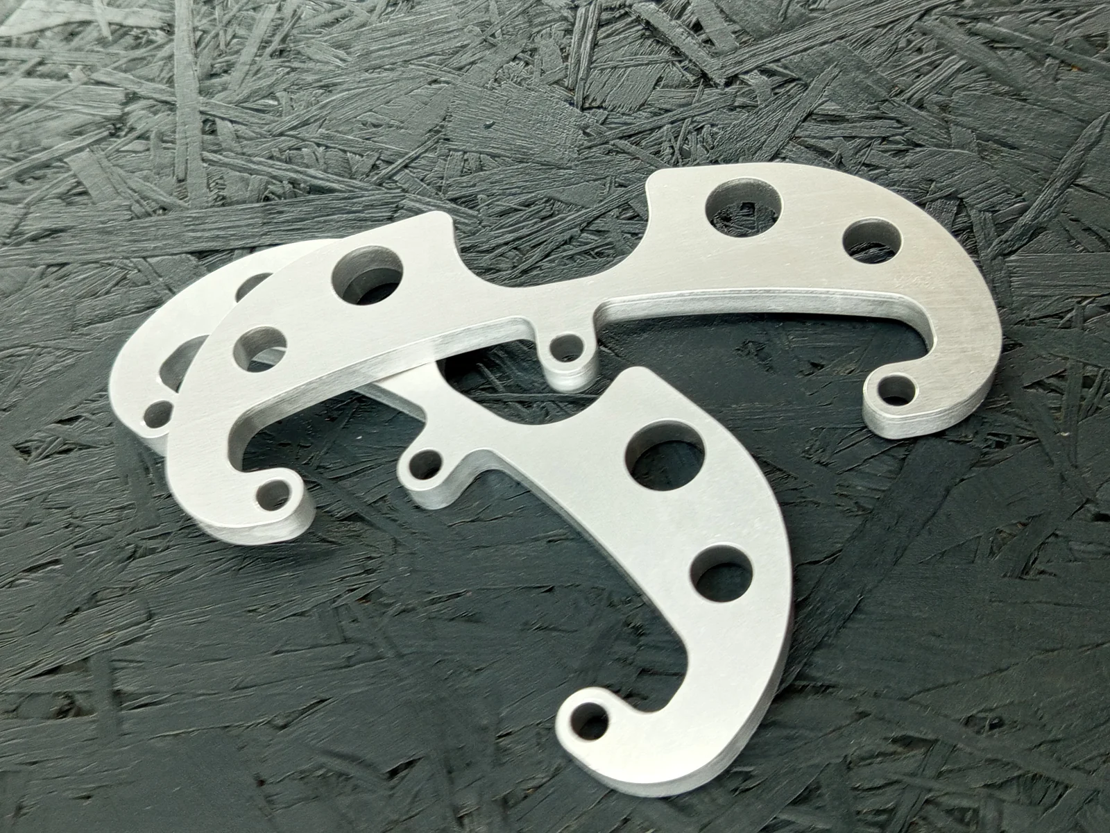 Zwei CNC-gefräste Halter aus Aluminium 5083, 8mm dick, mit mehreren Bohrungen und einer komplexen Kontur, auf dunklem Hintergrund.