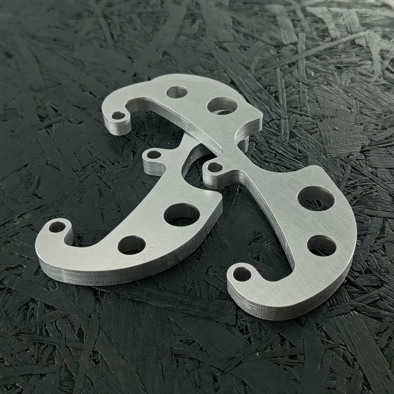 Zwei CNC-gefräste Halter aus Aluminium 5083, 8mm dick, mit mehreren Bohrungen und einer komplexen Kontur, auf dunklem Hintergrund.