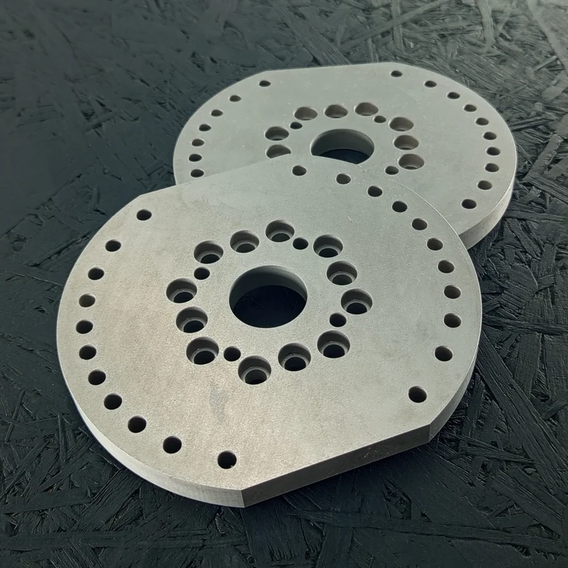 Zwei CNC-gefräste Adapterplatten aus Alu 7075, 10mm dick, mit vielen Bohrungen, auf dunklem Hintergrund.