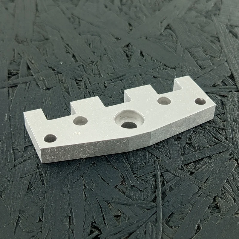 Nahaufnahme eines silbernen, CNC-gefrästen Flansches aus Aluminium 5083 mit Senkung, Bohrungen und komplexer Kontur auf dunklem Hintergrund.