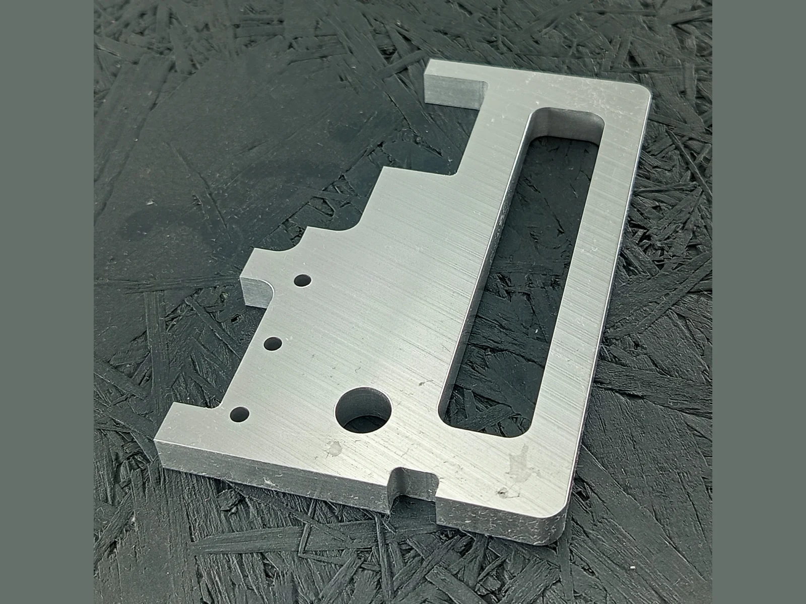 CNC-gefräster Halter aus Aluminium 5083, 10mm dick, mit Langloch und Bohrungen, auf dunklem Hintergrund.
