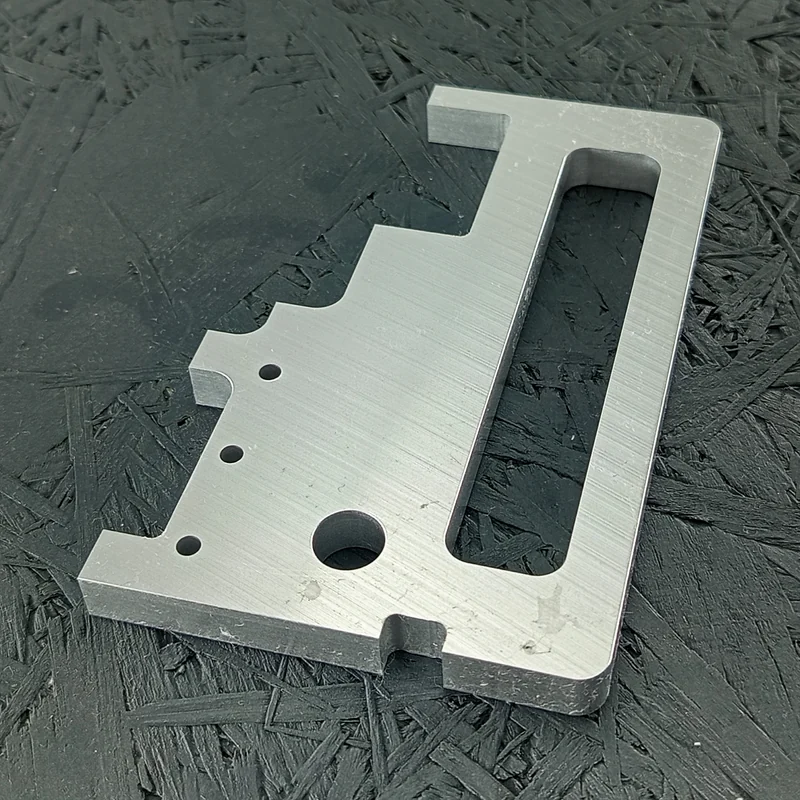 CNC-gefräster Halter aus Aluminium 5083, 10mm dick, mit Langloch und Bohrungen, auf dunklem Hintergrund.