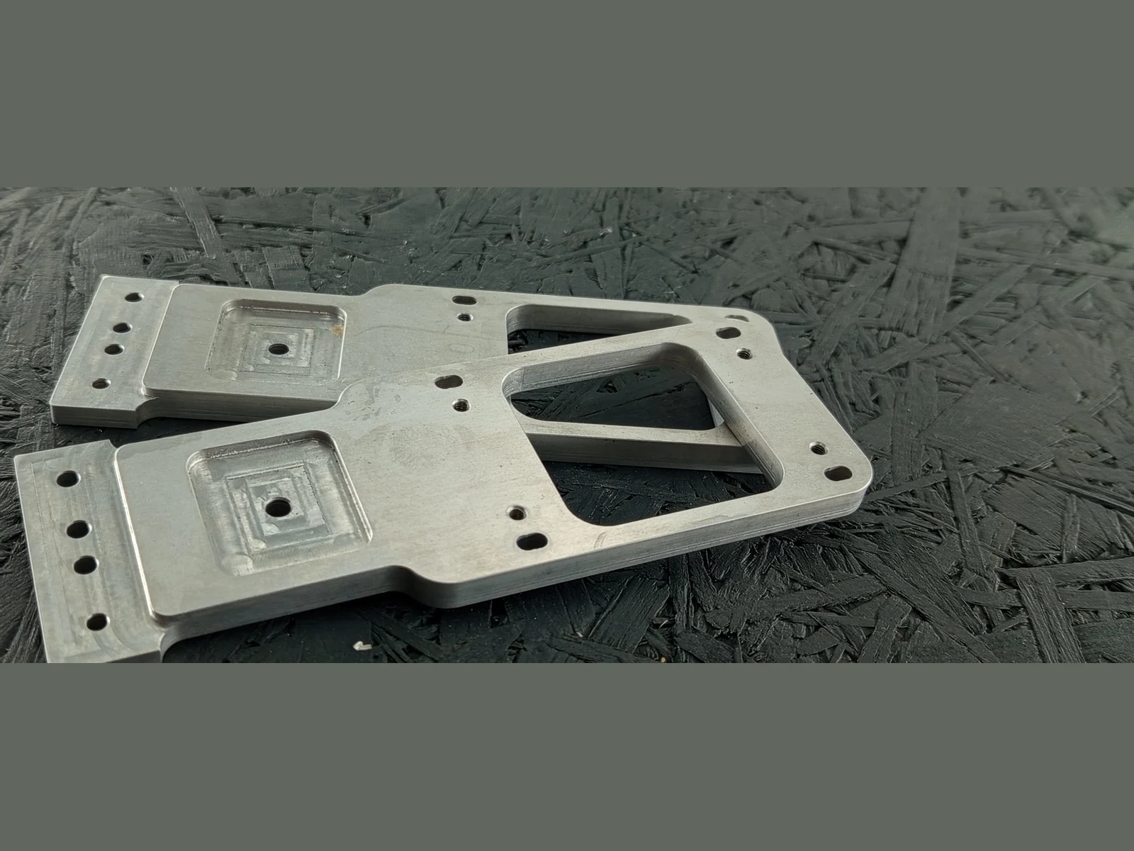 Zwei CNC-gefräste Adapterplatten aus Alu 7075 mit Bohrungen, Langlöchern und Senkungen auf dunklem Untergrund