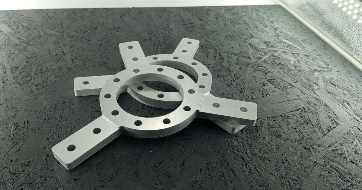 Zwei CNC-fräsgefräste Adapterplatten aus Alu 5083 auf dunklem Untergrund, mit zentraler Bohrung und vier Anschlussarmen